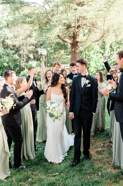 A newlywed couple holding hands with their wedding parties celebrating all around them