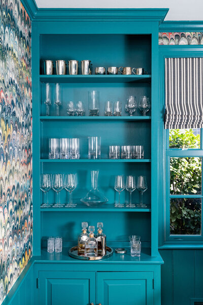 Teal blue dining room side board with bold wallpaper and barware
