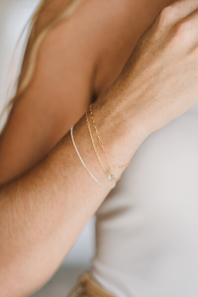 Stack of dainty gold and silver bracelets on wrist, featuring a small bezel-set charm.