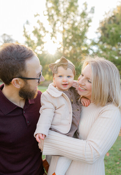 Parents snuggle close holding their toddler while she smiles, photographed outdoors by a Worcester family photographer.