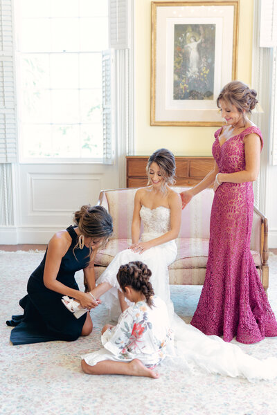 Sister helps bride get into wedding day shoes with mom looking on. Thomas Bennett House wedding. Mother of the bride gown.