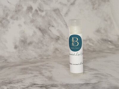 Original lip balm tube standing on marble stand with berry and balm logo