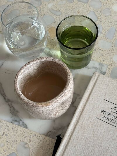 Journal with cups of green juice and water on a countertop, representing mindful nutrition, wellness, and healthy habits at Love Light Wellness Kauai