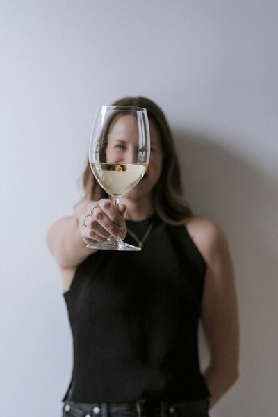 Woman cheers with a glass of wine, her smile radiating joy and celebration.
