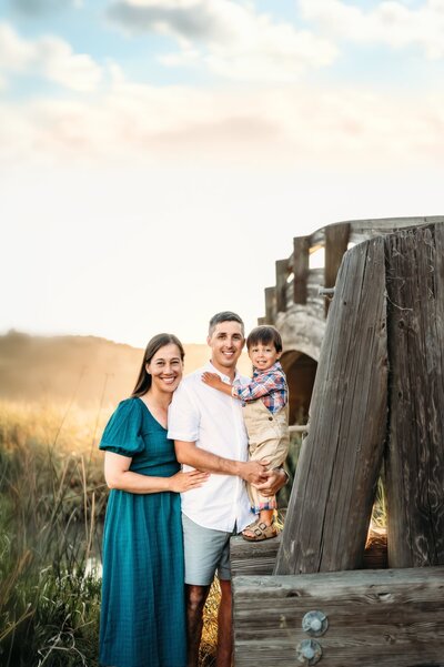 mom dad and toddler in walnut creek area for family photos. the sun is behind them and they are near a arch bridge