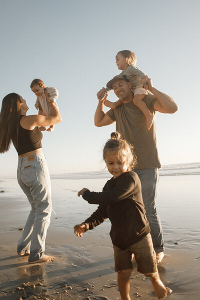 mom and dad play with their three children on the beach in san diego for family photos