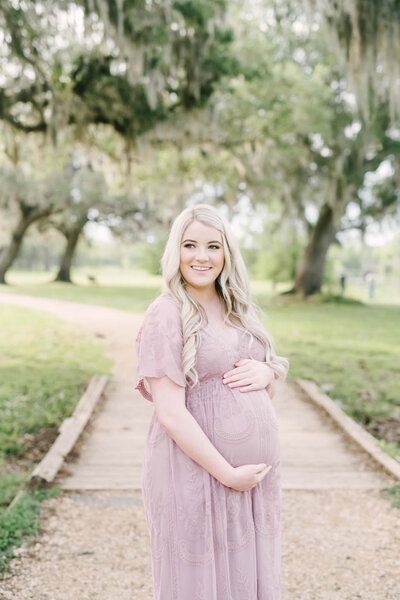 Blonde woman in pink gown smiles and poses for maternity portrait
