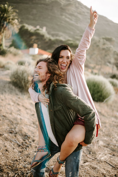 Couple in California during their engagement session with the guy giving the girl a piggy back ride