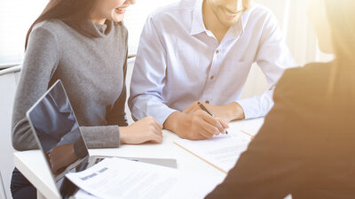 Image of a man and woman sitting at a desk with a certified public accountant. The couple is signing paperwork.