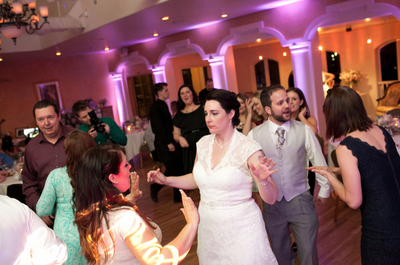 Envision columnated beams of rose colored up lighting providing a  background canvas for an elated  bride and groom dancing to the beats of their DJs playing to a packed dance floor of guests.