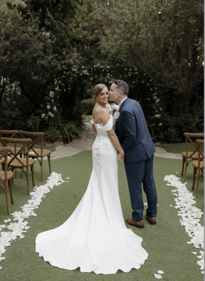 groom leans in to kiss brides cheek on ceremony aisle