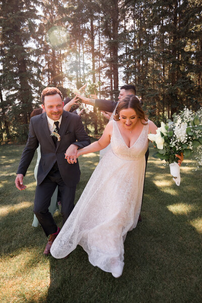 Bride & groom running through field on wedding day, golden sun flaring overhead