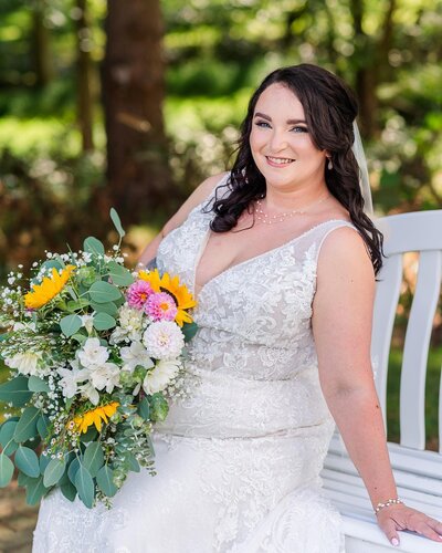 A bride holding a bouquet of flowers sitting on a bench.