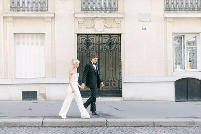 A bride and groom walking hand in hand down a street in Paris.