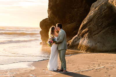 A bride and groom kiss  on the beach during their Oregon coast elopement.
