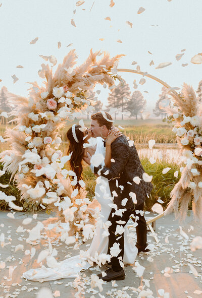 bride and groom kissing while flower petals fall around them