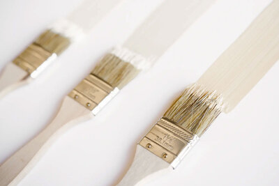 image showing three wooden paint brushes loaded with off white paint on a white background