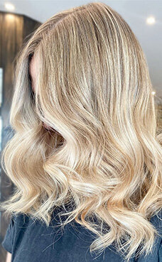 Soft blonde waves with luminous shine and subtle balayage, displayed in a professional salon setting.