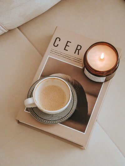 A magazine sitting on a cream leather sofa with a cup of tea and a candle on top