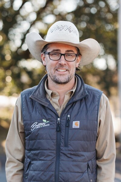 David Munsey III smiling in a cowboy hat and dark shirt outdoors, representing Better Lawns and Gardens in Little Rock, Arkansas.
