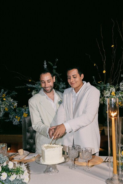 A gay couple in white suits cutting their wedding cake