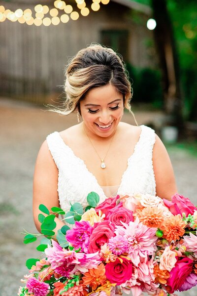 Bride smiling at her flowers that are pink, yellow and orange