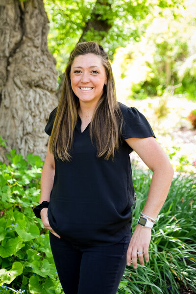 Colorado photographer, Sarah Mcnew, smiles at the camera in a summery, green setting.