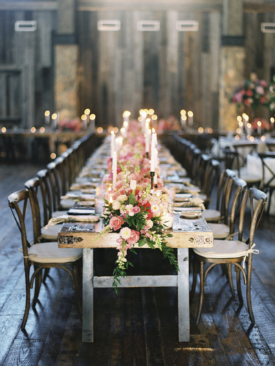 A long dining table seating more than 20, looking down the long side where a huge table garland runner of flowers and candles decorate the moody room.