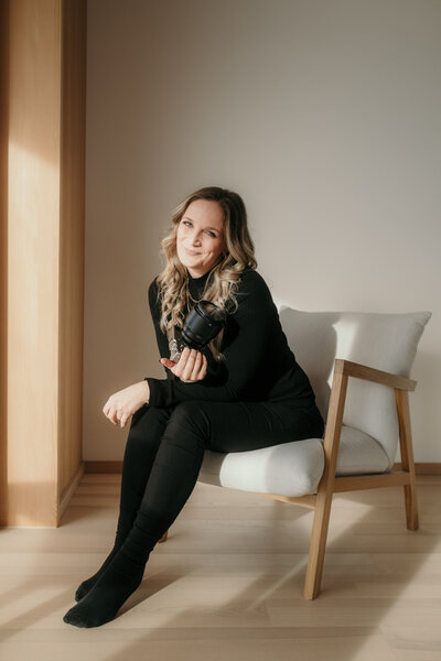 Karin Busch, Hochzeitsfotografin, sitzt lächelnd mit Kamera auf einem Sessel