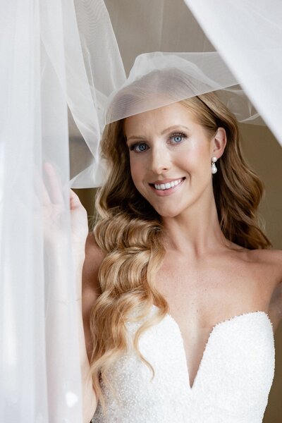 Bride standing in ballroom holding bridal bouquet looking out window