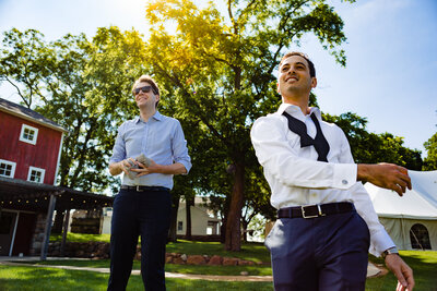 A groom playing cornhole with his bowtie undone at the barn at Cornman Farms in Dexter Michigan