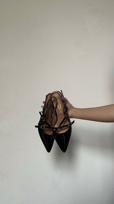A woman's hand holding one pair of high heels. The heels are black with straps.
