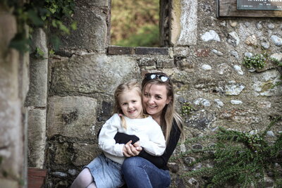 Young girl and mother cuddling in front of an old wall manor barn bexhill