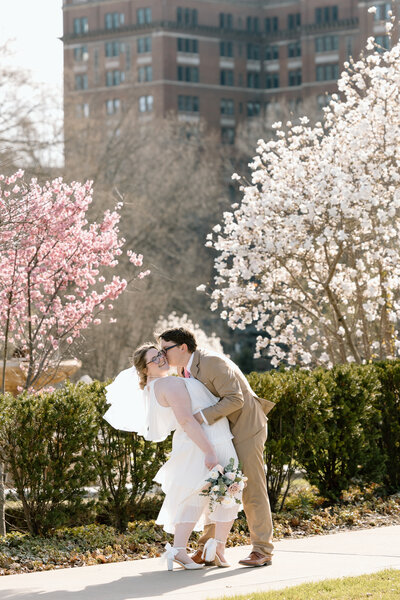 Bride and groom in front of pink and white blossoming trees.