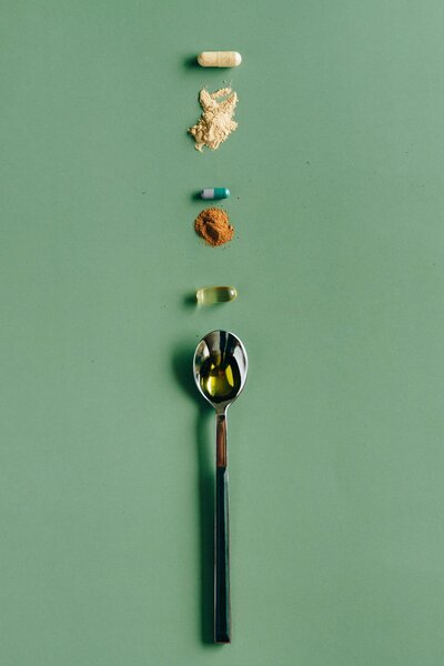 spoon, vitamins and other wellness items in green back ground