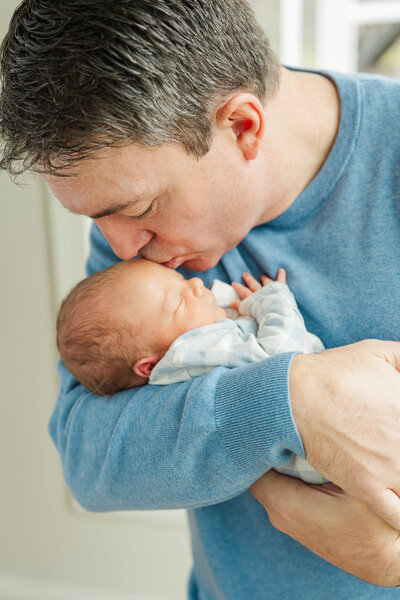 a father kisses his newborn on the head while holding him in his arms
