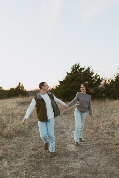 A couple running towards the camera, laughing and smiling at each other with pure happiness and connection, capturing a carefree and joyful moment.