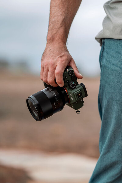 Close-up of Joseph Mayden holding a Sony mirrorless camera with a professional lens, showcasing the gear used for high-quality photo and video production.