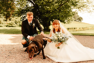bride and groom kneeling down to have their photograph taken with their dog
