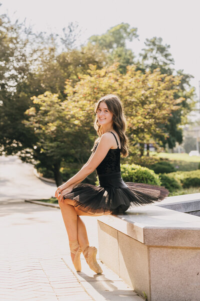 Dancer in a black leotard and tutu sitting on the edge of a fountain at Belmont University.