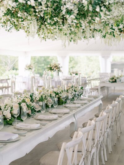 Wedding reception in a white tent with the ceiling covered in white and pink flowers and greenery