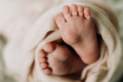 Close-up detail of tiny newborn feet wrapped in a soft beige blanket, capturing the delicate wrinkles and toes of a sleeping baby.