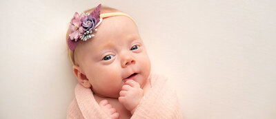 Newborn Baby with rust colored swaddle blankets sleeps on belly