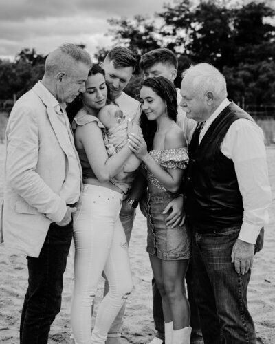 Large family photo in black and white standing closely together looking at baby boy in Annapolis Maryland
