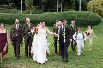 A newlywed couple laughing as they walk with their wedding party 