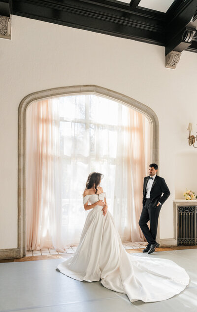A groom admiring his bride on their wedding day as she shows him her gown.