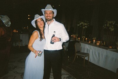 Flash film photo of couple wearing cowboy hats and holding drinks at reception