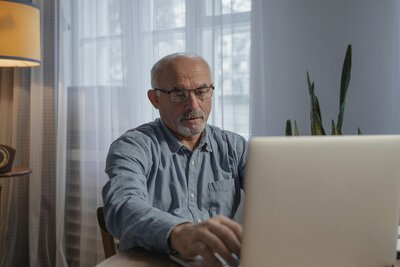 An older man working on a laptop, looking slightly frustrated