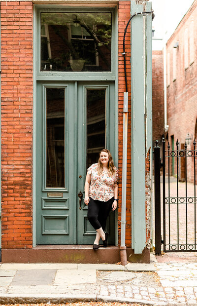 Image of woman leaning agains a brick building with green painted trim in the city