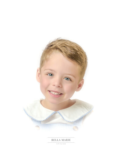 Little boy with sandy brown  hair and blue eyes smiling for his heirloom portrait, wearing blue and white.